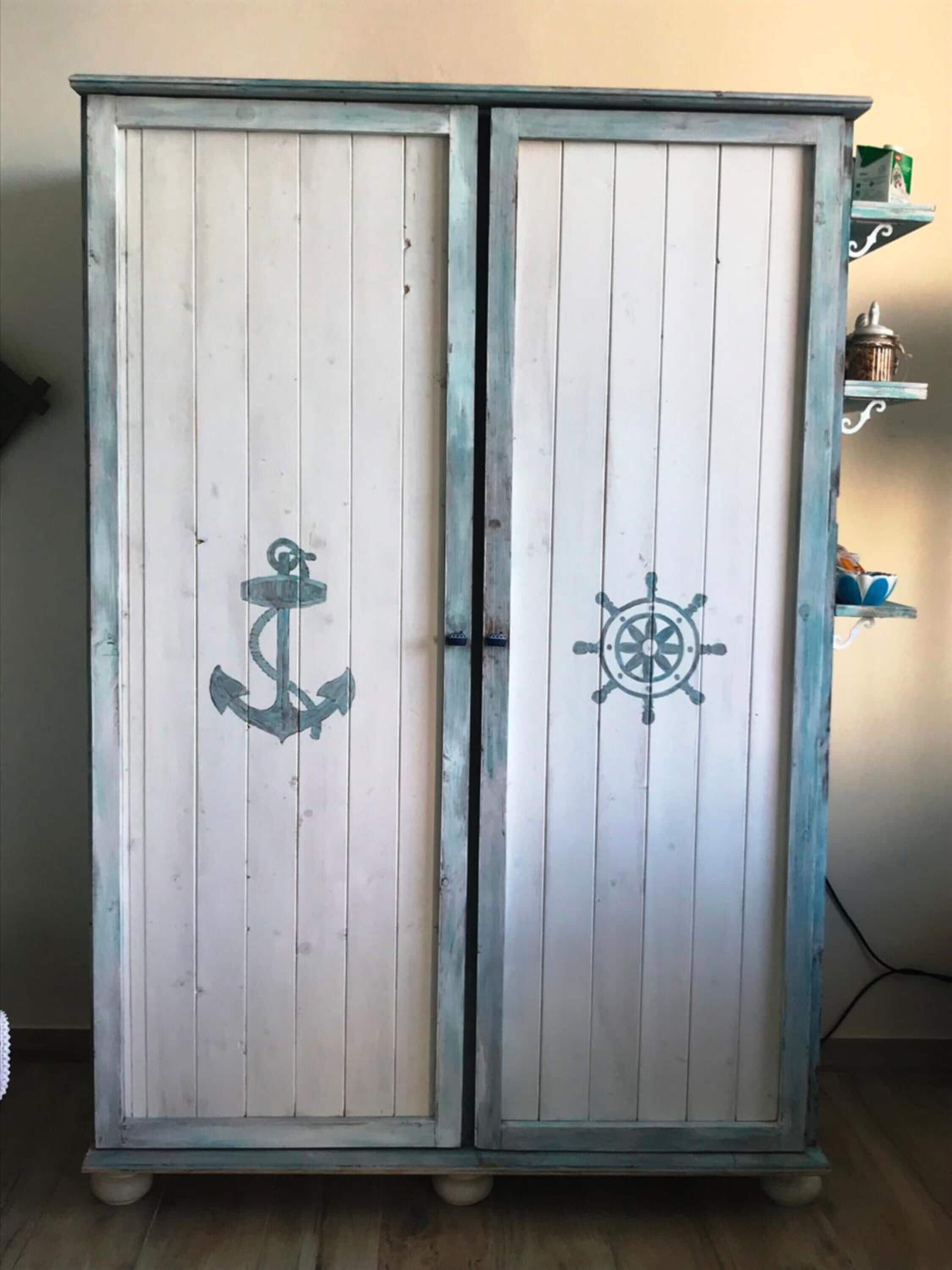 Un mueble blanco de madera con temática náutica, que presenta un ancla y un timón.