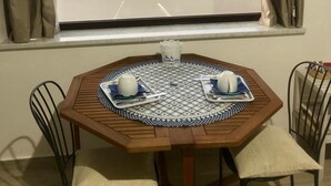 Comedor con una mesa preparada para dos personas, una ventana con cortinas y vistas al mar y a la vegetación.