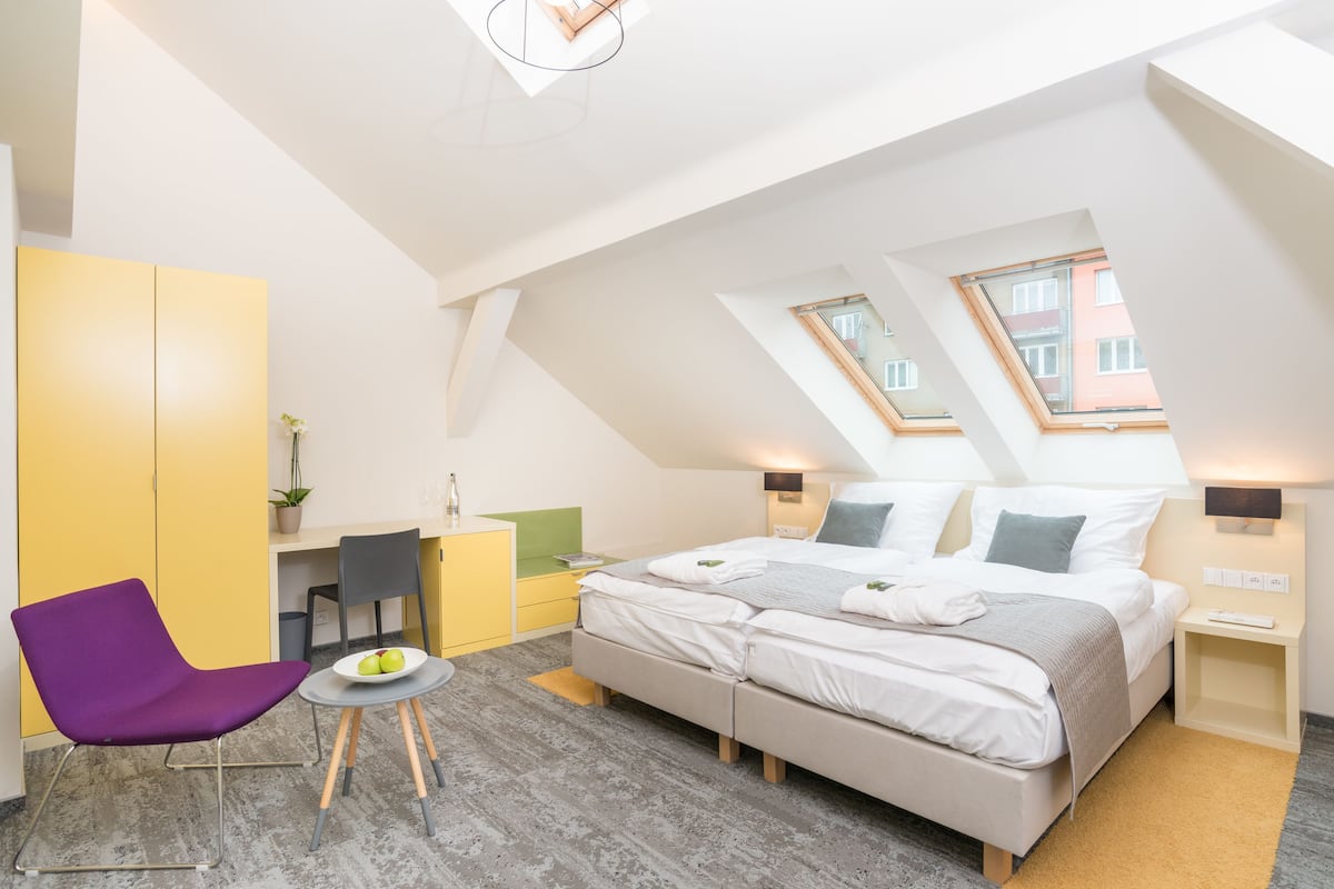 A modern bedroom with a large bed, a desk, a chair, and two skylights.