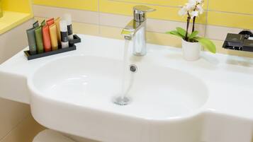 A bathroom sink with a chrome faucet, a potted orchid, and a soap dispenser holder.