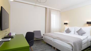 A hotel room with a bed, a desk, a chair, a TV, and a window with curtains.