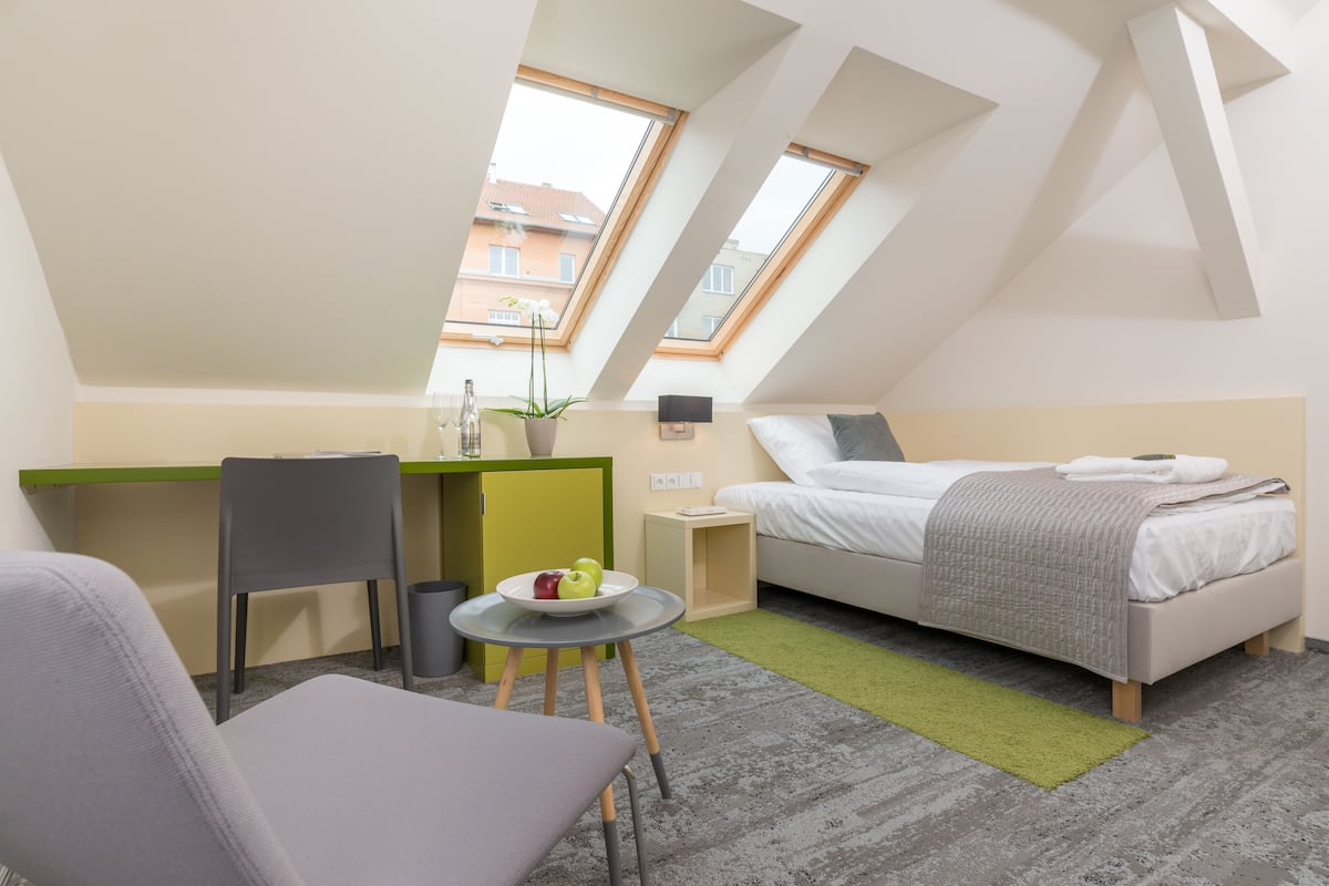 A modern, compact room with a bed, a desk, and a chair. There are two skylights providing natural light.