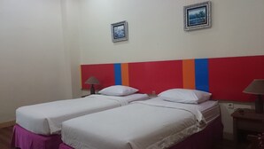 A hotel room with two single beds, a red-striped headboard, two small framed pictures on the wall, and a nightstand with a lamp. - Hotel Limoes (Mataram)