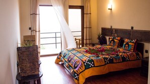 A bedroom with a large bed, a chair, a window with curtains, and a wall-mounted light.