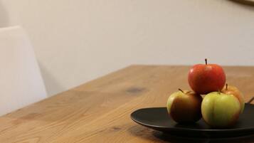 Una mesa de madera con un plato negro que contiene tres manzanas.