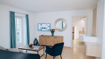 Een moderne woonkamer met een houten kast, een zwarte stoel, een salontafel met een fruitschaal en een aan de muur bevestigde televisie.