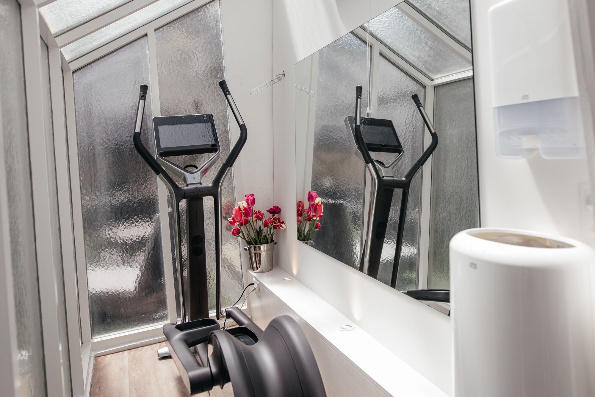 Un gimnasio con equipo de ejercicio, una ventana con vidrio esmerilado y un jarrón con flores.