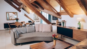 A modern loft with exposed wooden beams, a curved sofa, a wooden dining table, and a kitchen area.