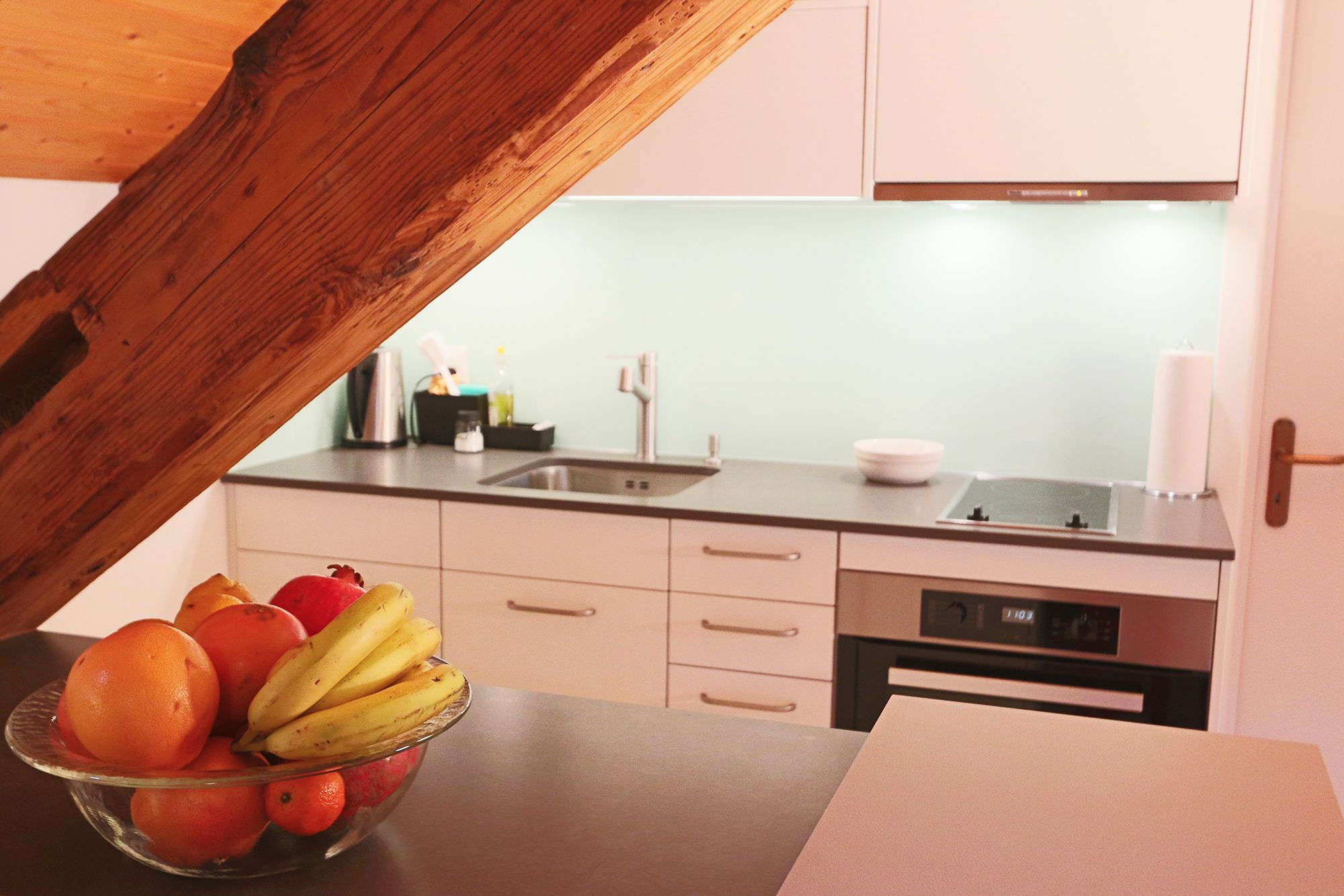 A kitchen with a wooden ceiling, a sink, a stove, and a dishwasher. There is a bowl of fruit on the counter.