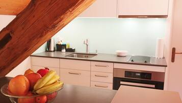 A kitchen with a wooden ceiling, a sink, a stove, and a dishwasher. There is a bowl of fruit on the counter.
