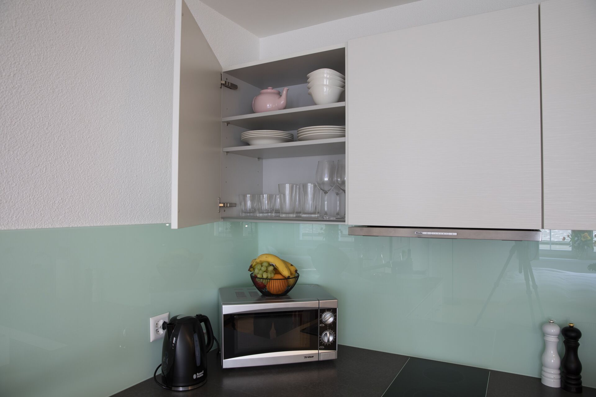 A compact kitchen with a microwave, a kettle, and a bowl of fruit on the counter.