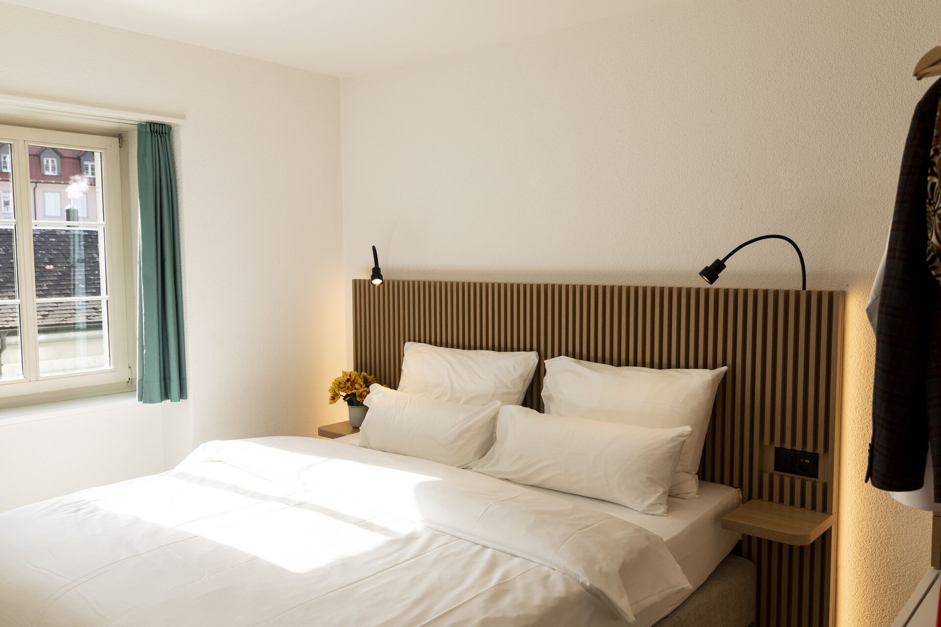 A hotel room with a bed, a nightstand, a lamp, and a window with curtains.