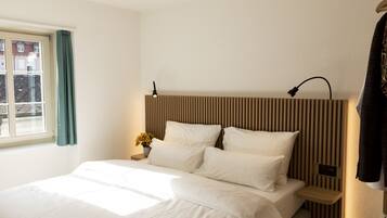 A hotel room with a bed, a nightstand, a lamp, and a window with curtains.