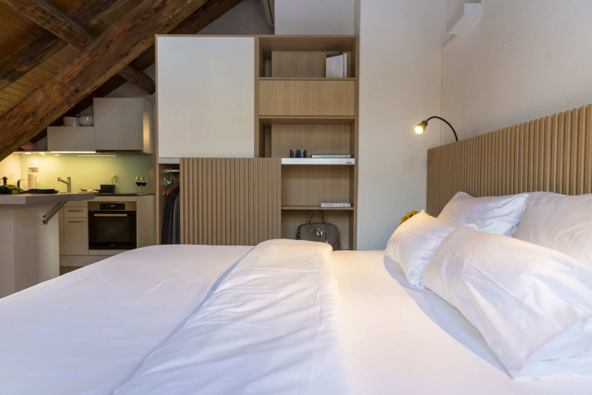 Une chambre à coucher avec un grand lit, une tête de lit en bois et des étagères intégrées où sont disposés des livres et des objets décoratifs.