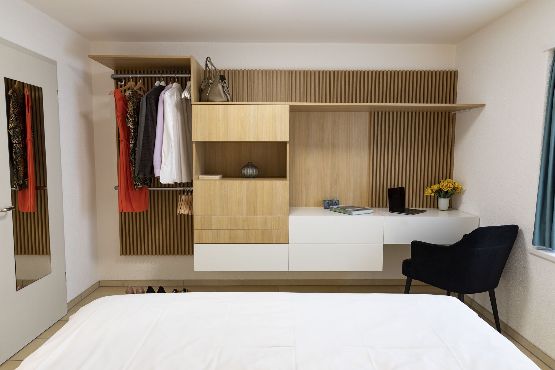A modern bedroom with a bed, a built-in wardrobe, a desk with a chair, and a window with curtains.