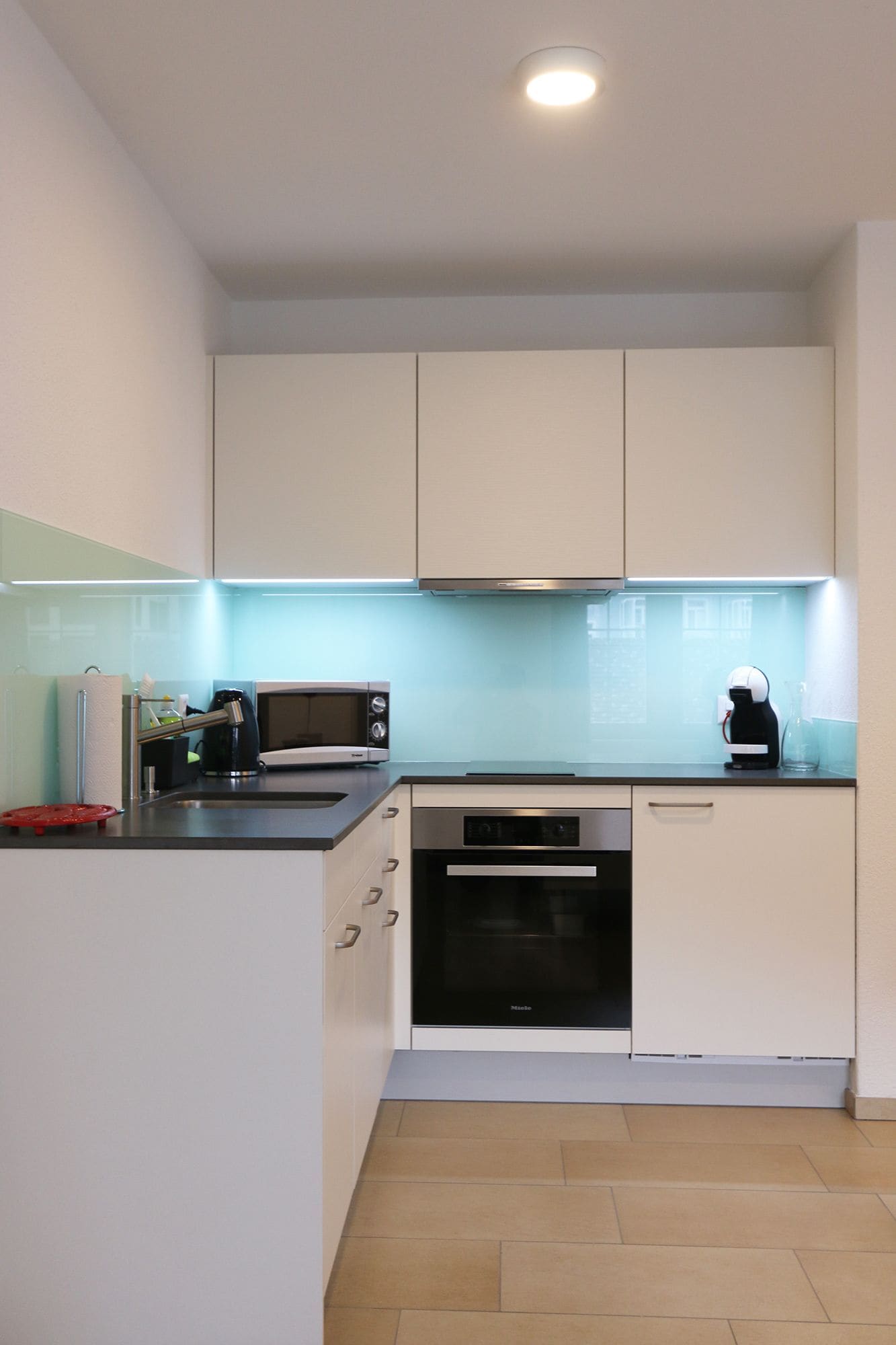 Una cocina moderna con armarios blancos, microondas, cafetera y horno empotrado.