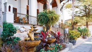 Un edificio con una escalera de piedra, una fuente decorativa con un dragón dorado y varias plantas en macetas.