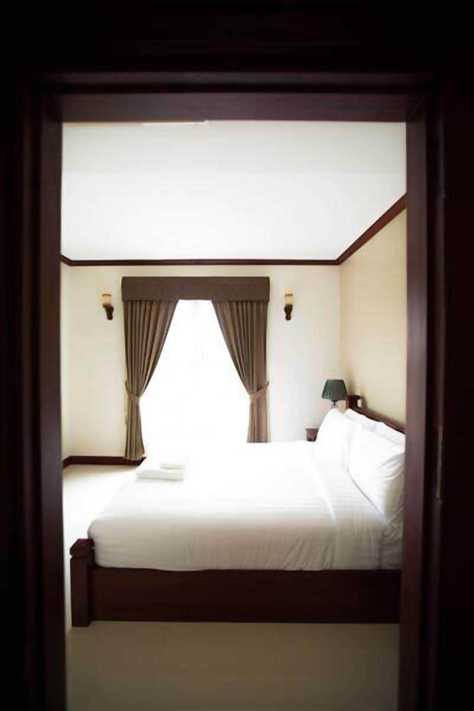 A hotel room with a large bed, curtains, a bedside lamp, and a nightstand.