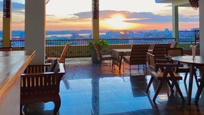 Una terraza en la azotea con mobiliario y vistas a la puesta de sol sobre la ciudad.