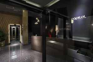Un moderno vestíbulo de hotel con recepción, zona de estar y un muro de vidrio que muestra el nombre del hotel.