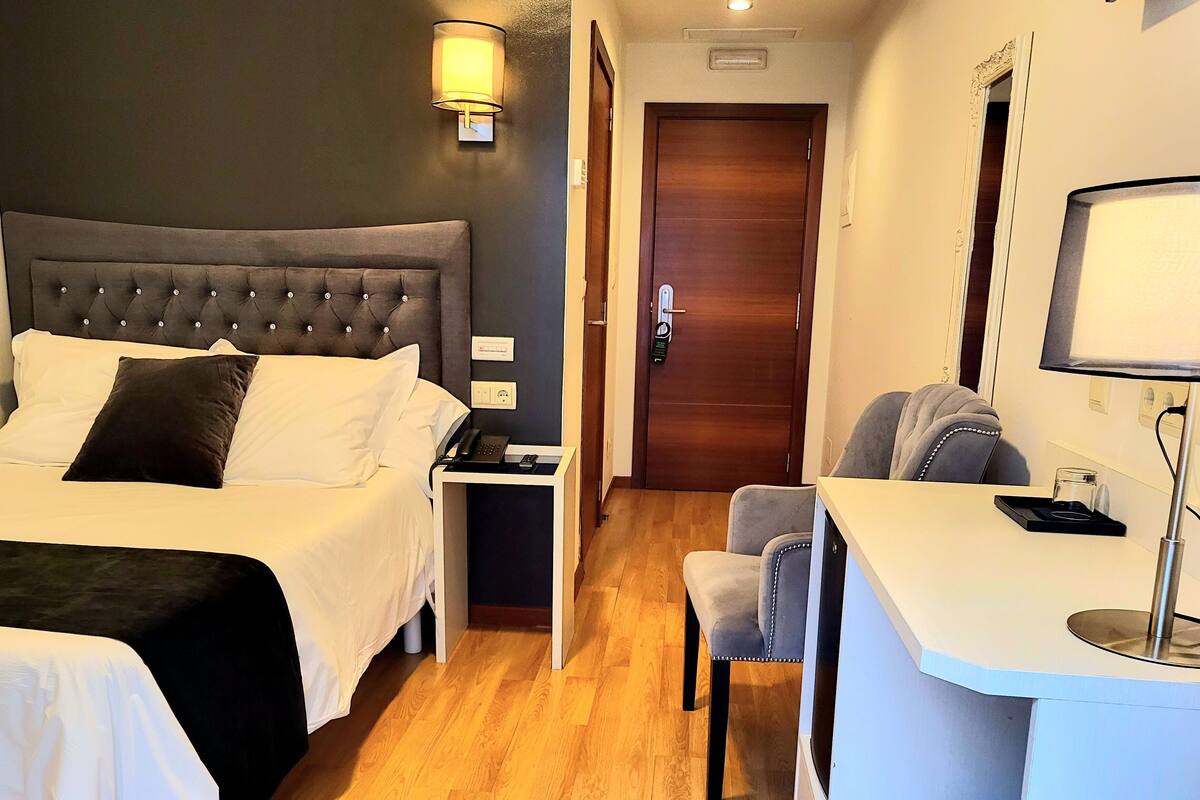 Une chambre d’hôtel comprenant un lit, une table de chevet, une lampe, une chaise, un bureau et une porte.