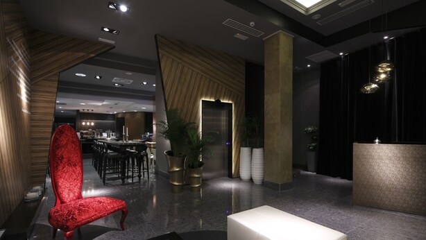 A modern lobby with a red upholstered chair, a reception desk, and a seating area with white ottomans. - Capitol Boutique Hotel (Santiago de Compostela)