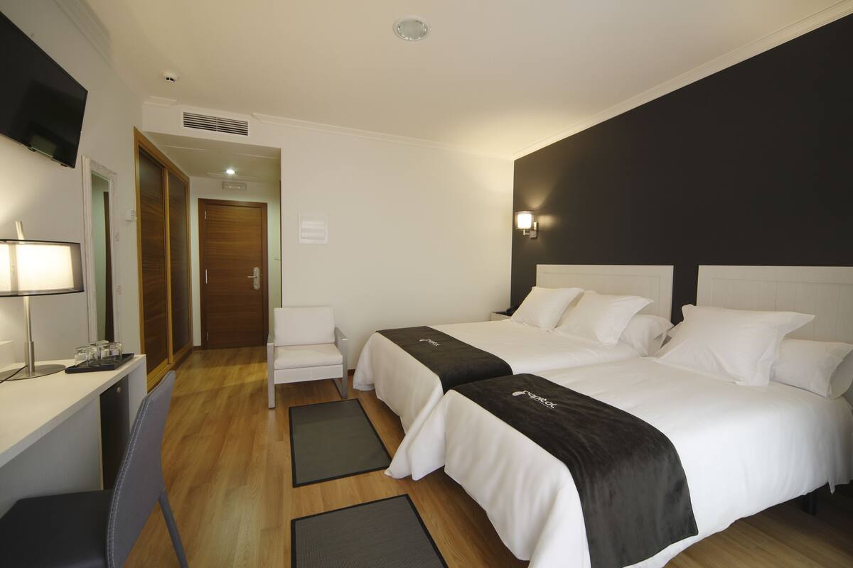Une chambre d’hôtel avec deux lits, un bureau avec une lampe, une chaise et un téléviseur fixé au mur.