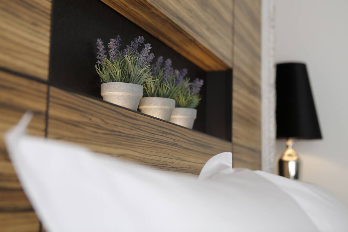 Une chambre moderne avec un mur d’accent en bois, un lit blanc et trois plantes en pot disposées sur une étagère.