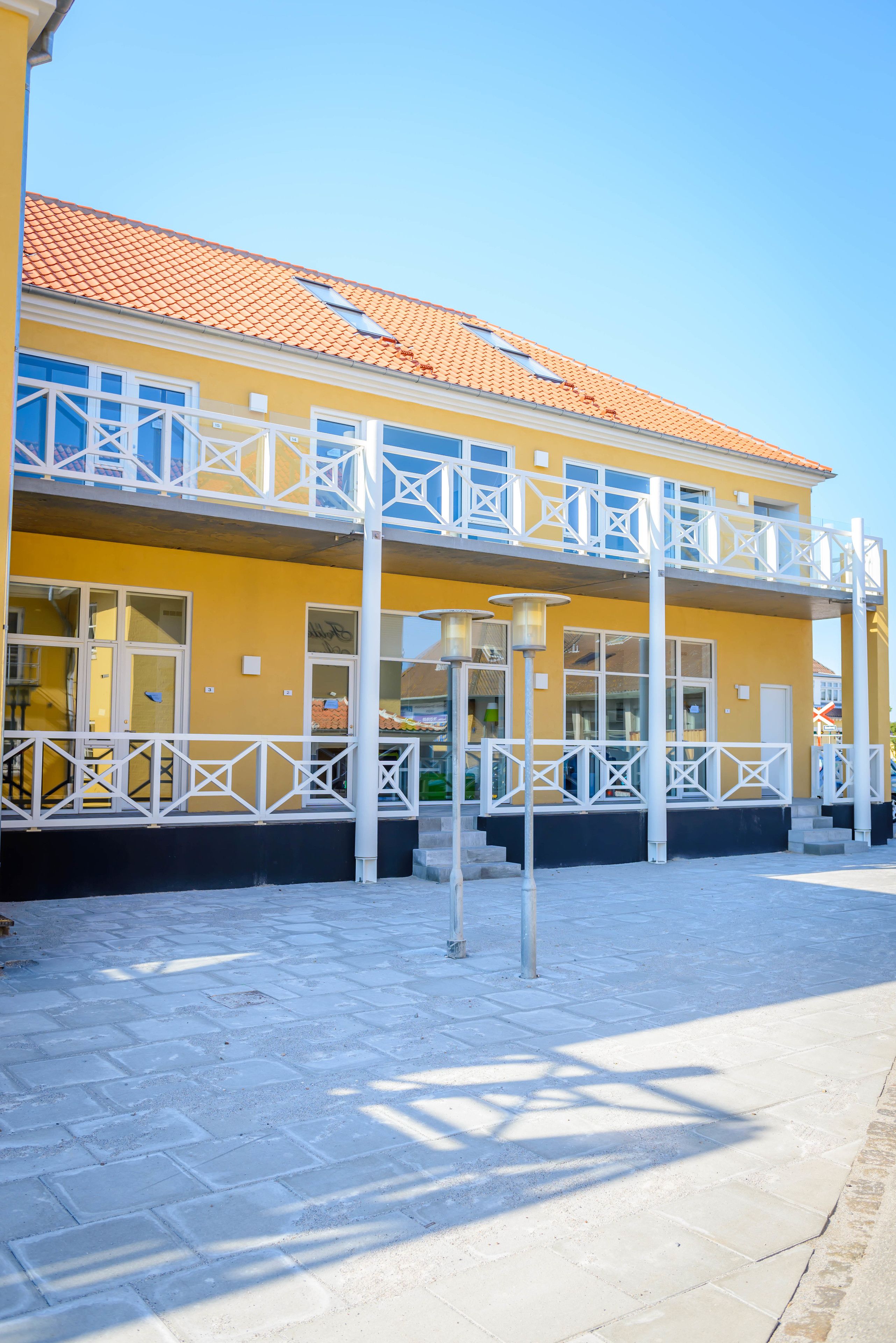 Een geel gebouw met een pannendak en witte hekwerken.