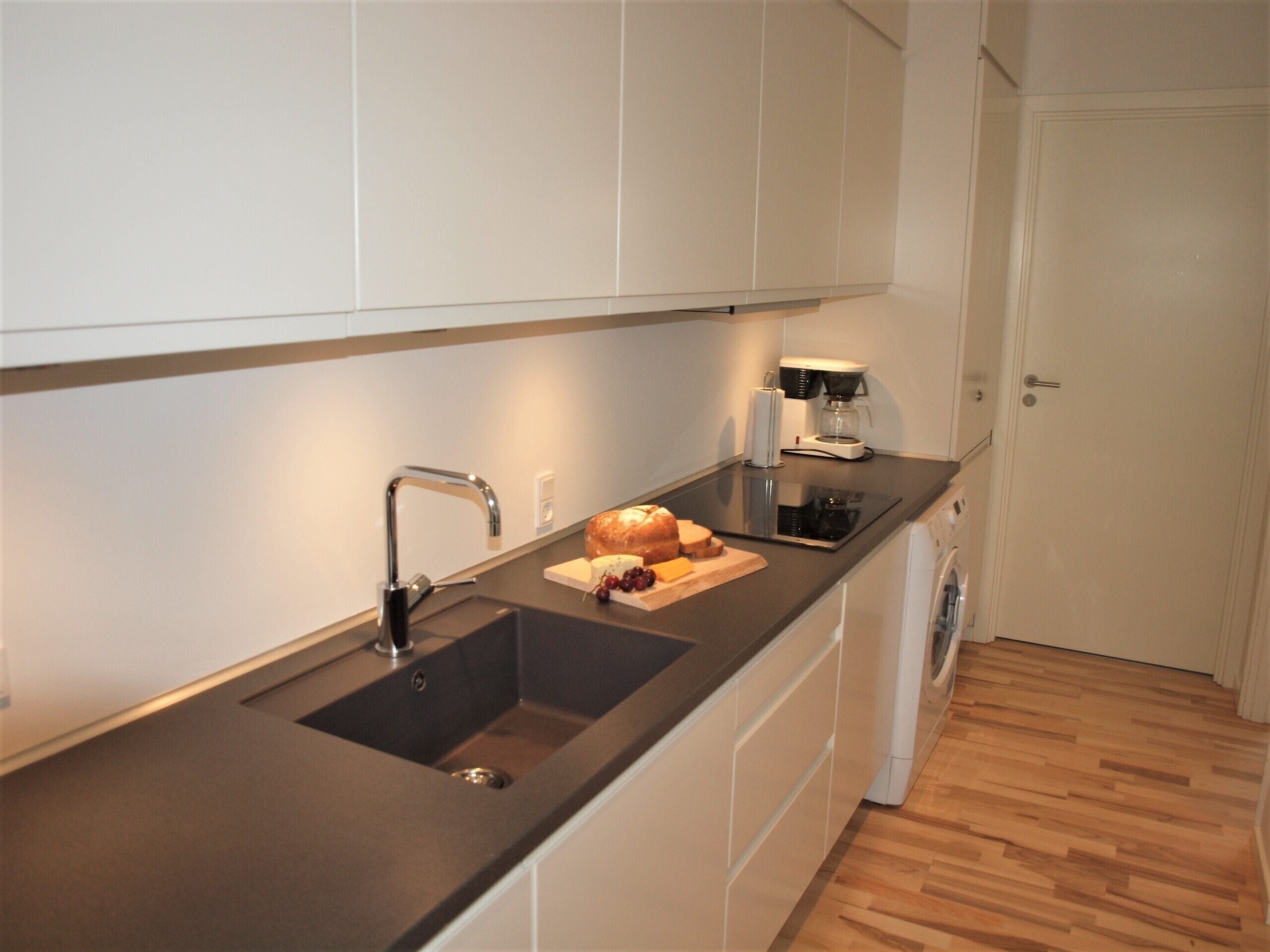 Una cocina moderna con un lavamanos doble, una cafetera y una barra de pan sobre la encimera.