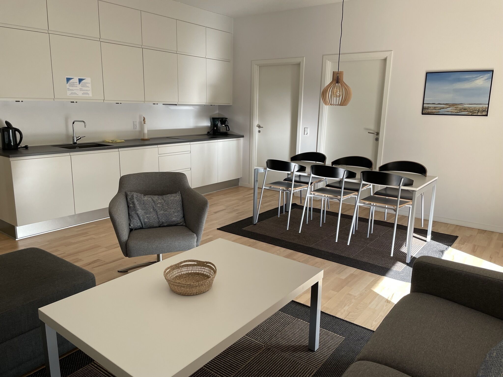 Eine moderne Küche mit weißen Schränken, ein Essbereich mit Tisch und Stühlen sowie ein grauer Sessel.