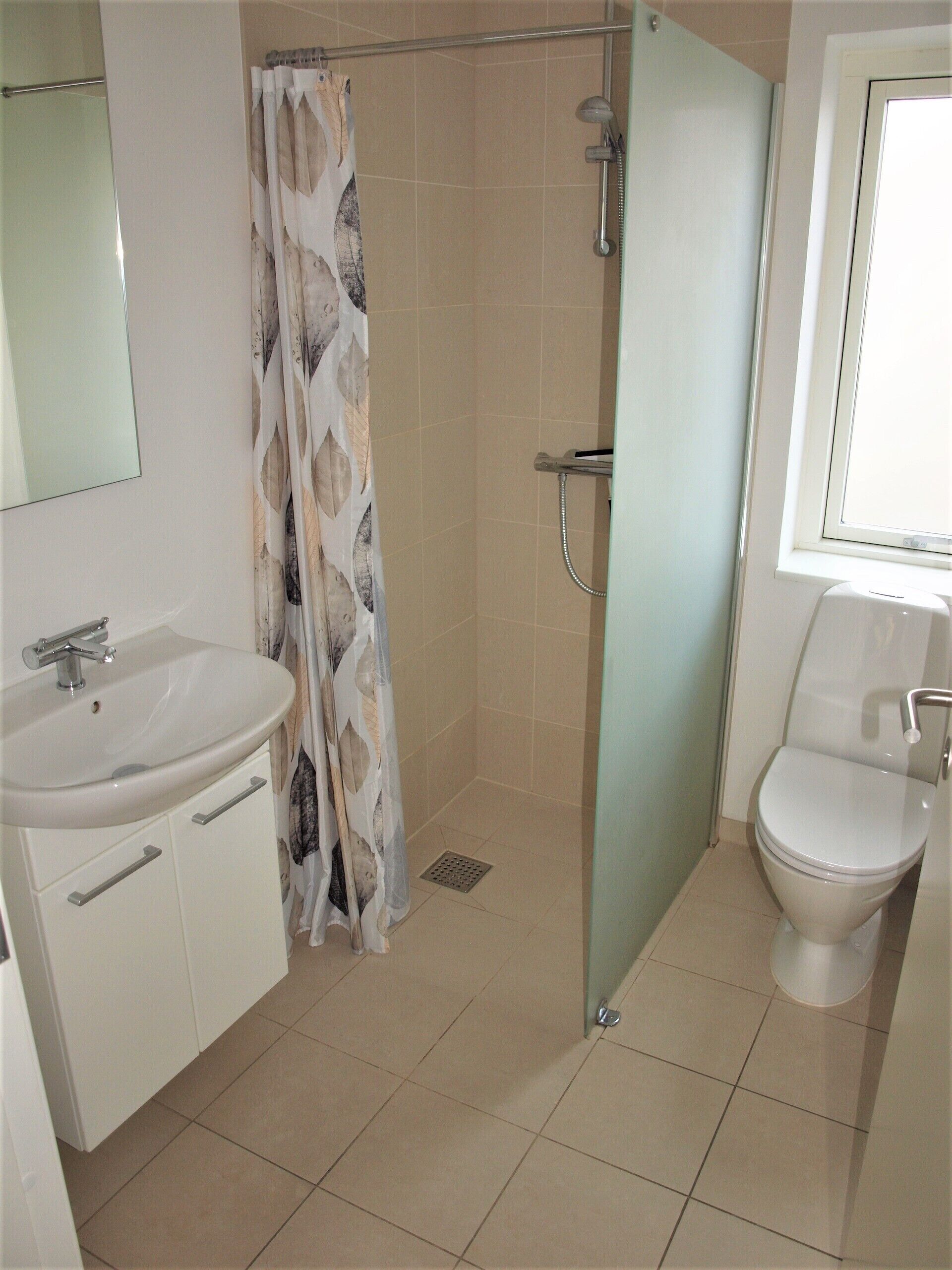 Een badkamer met douche, toilet, wastafel en spiegel.