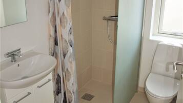 Een badkamer met douche, toilet, wastafel en spiegel.