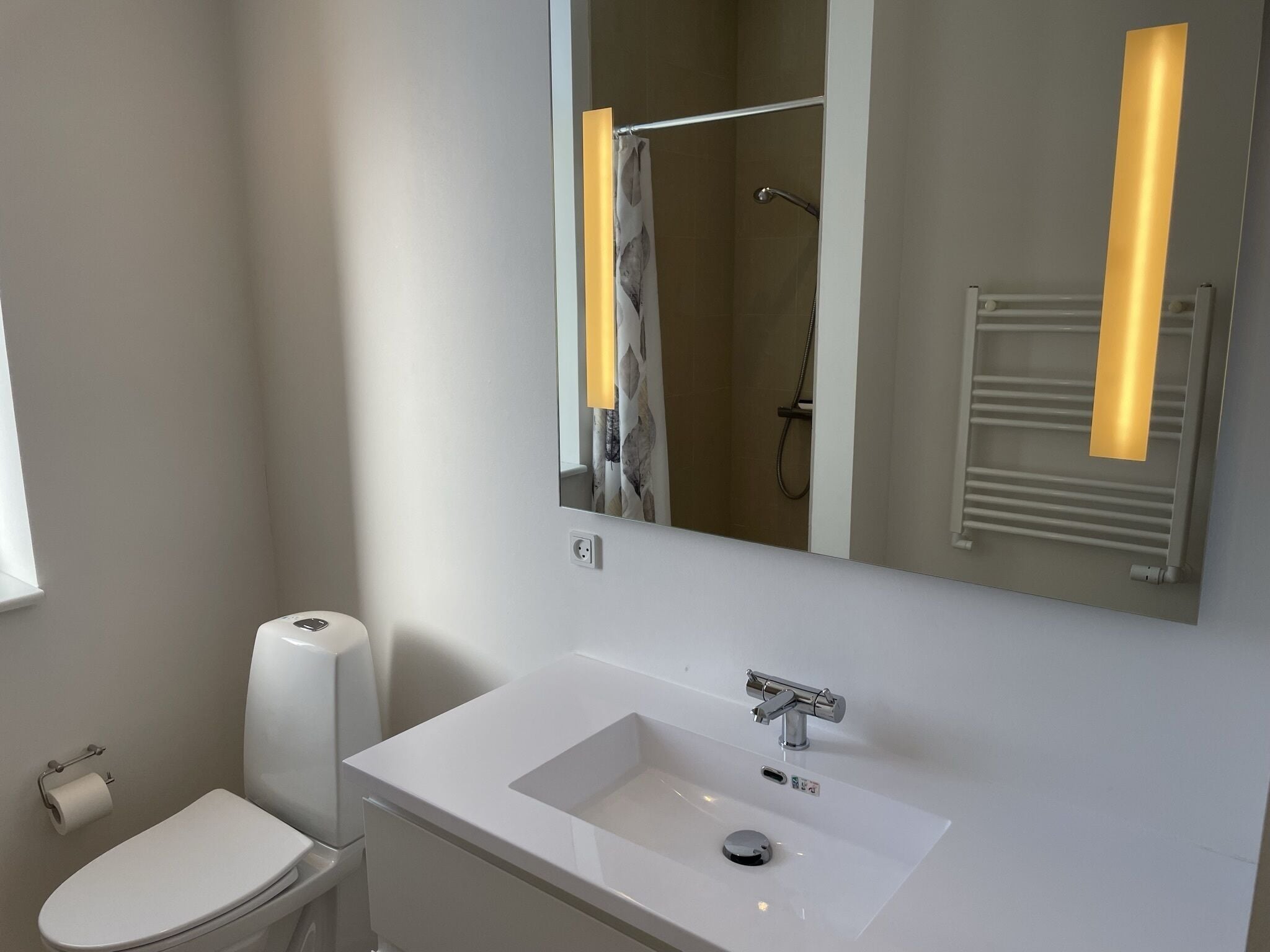 A modern bathroom with a white sink, a toilet, and a shower.