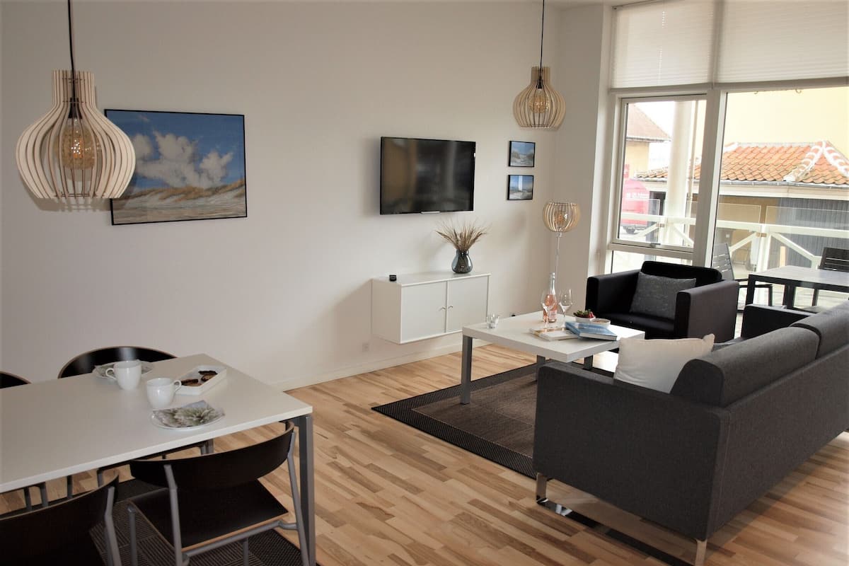 A modern living room with a sofa, dining table, chairs, and a TV mounted on the wall.