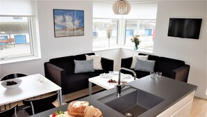A modern kitchen with a central island, black and white furniture, and a view of the outside. - Plesners Havnelejligheder (Skagen)