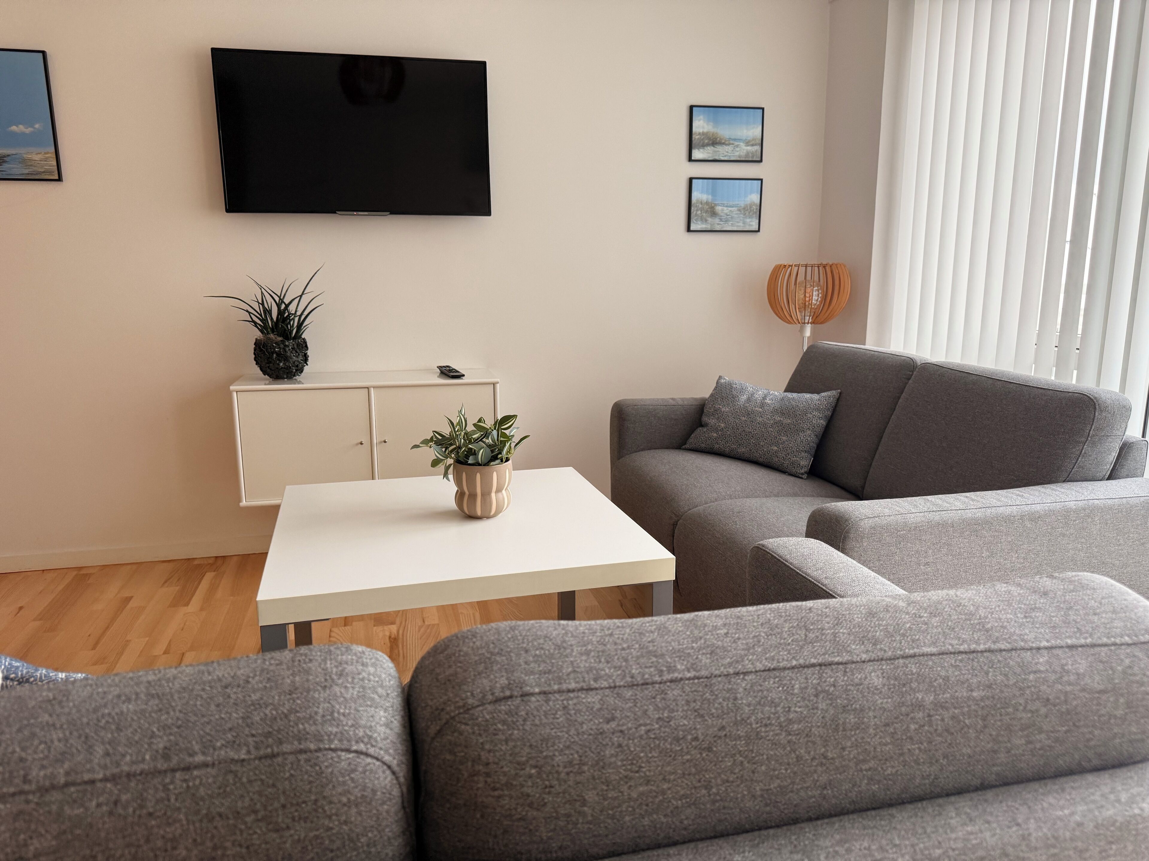 Ein modernes Wohnzimmer mit einem grauen Sofa, einem weißen Couchtisch und einem flachbildfernseher, der an der Wand befestigt ist.