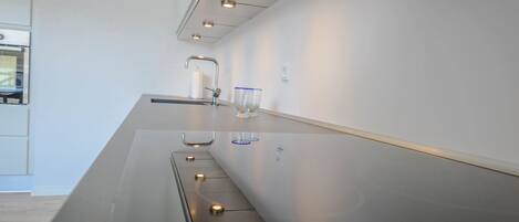 Una cocina moderna con una encimera amplia, horno empotrado e iluminación debajo de los armarios.