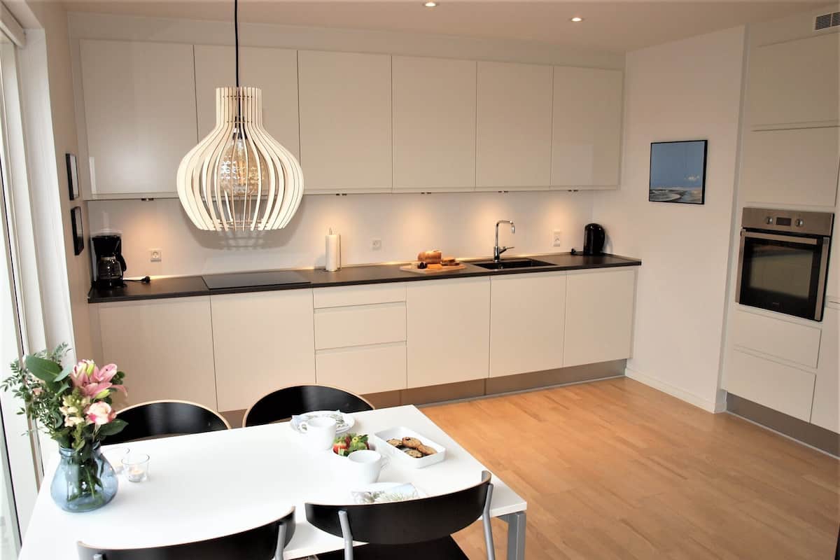 A modern kitchen with white cabinets, a black countertop, and a dining area with a white table and black chairs.