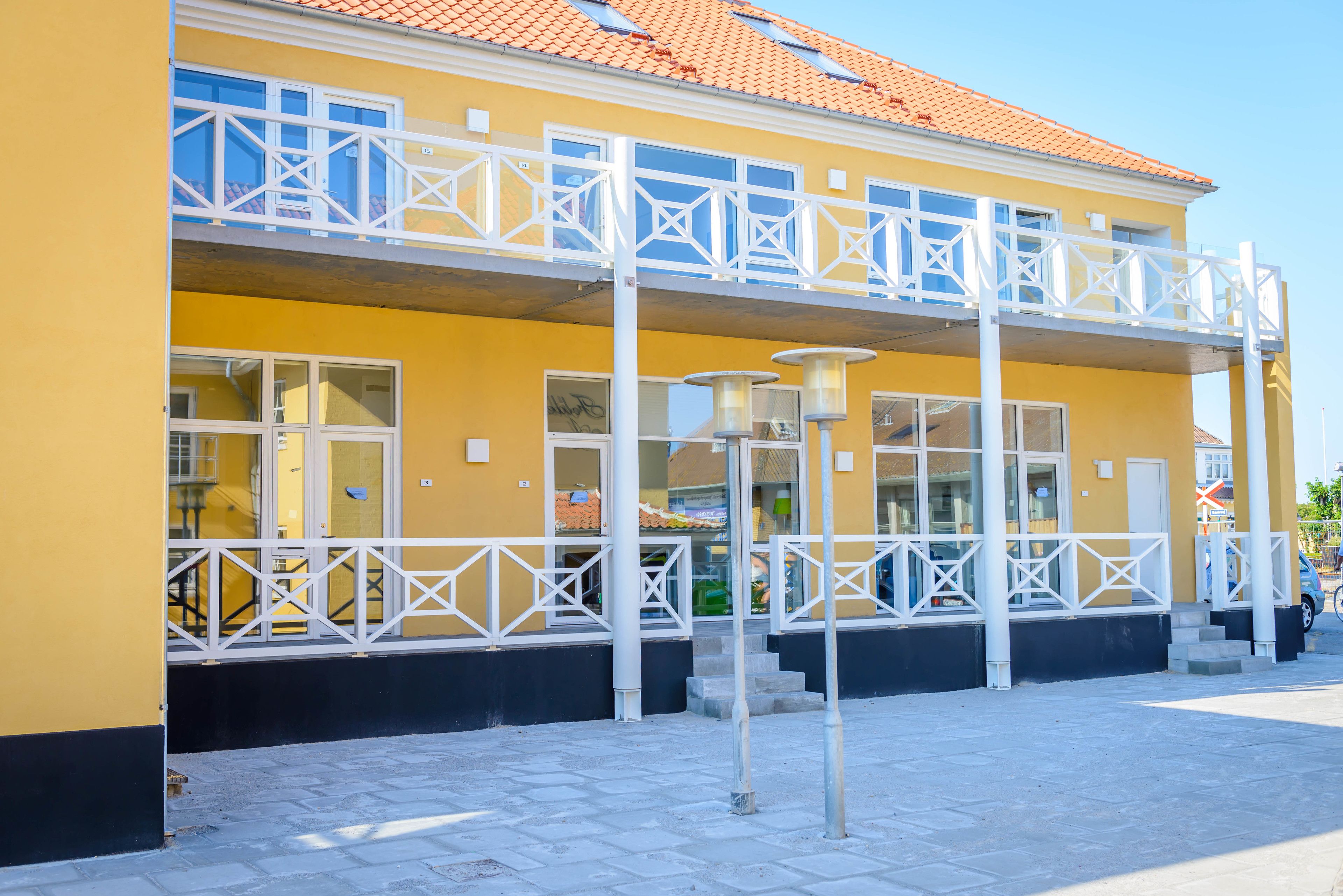 A yellow building with a balcony, large windows, and a tiled roof.