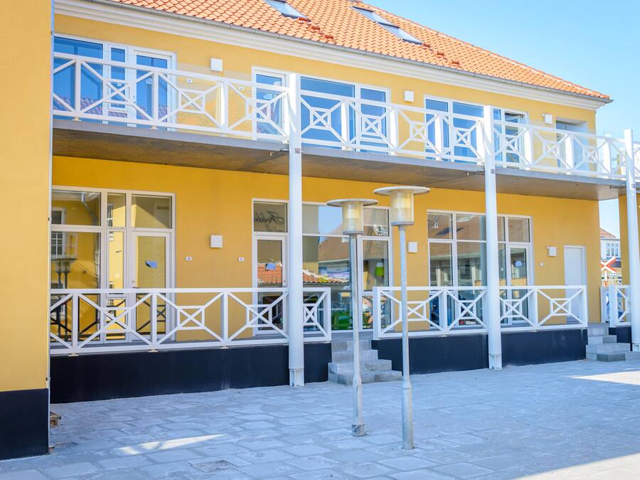A yellow building with a balcony, large windows, and a tiled roof.