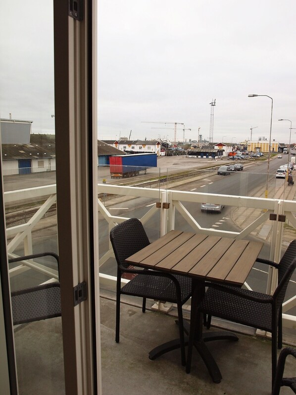 Un balcon avec une table et des chaises, donnant sur une rue animée où circulent des voitures et où se trouve une grue de chantier.