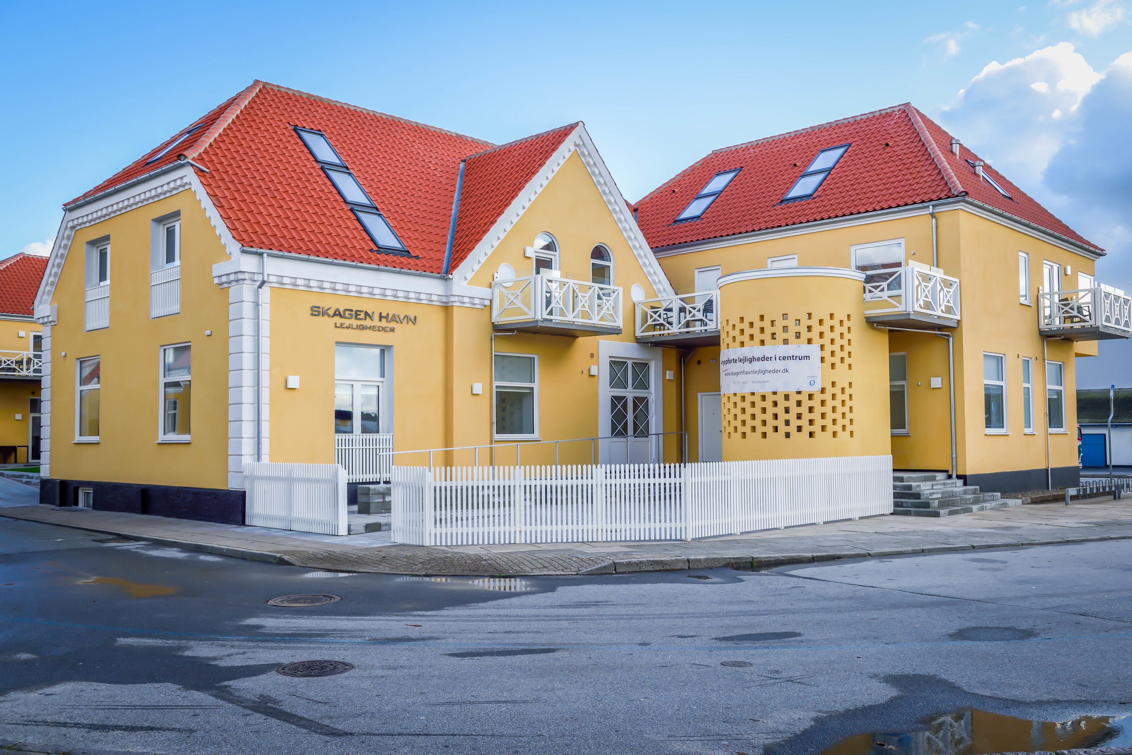 A yellow building with red roofs and white balconies, labeled "Skagen Havn Lejlighed."