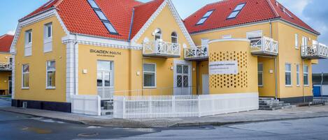 A yellow building with red roofs and white balconies, labeled "Skagen Havn Lejlighed."