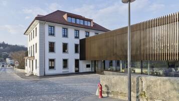 Ein modernes Gebäude mit weißer Fassade und geneigtem Dach, neben einer Holzkonstruktion mit senkrechten Paneelen.