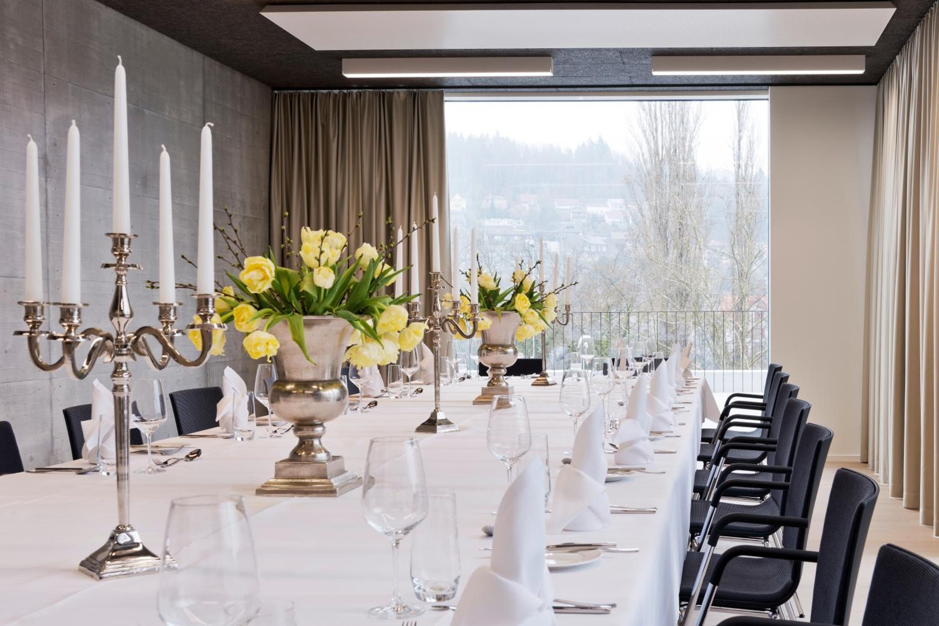 Una larga mesa de comedor dispuesta para un evento formal, con manteles blancos, candelabros de plata y flores amarillas.