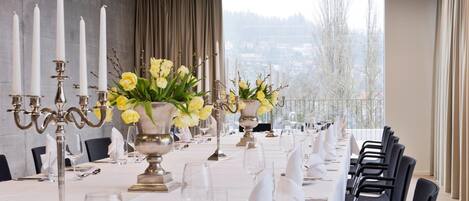 Una larga mesa de comedor dispuesta para un evento formal, con manteles blancos, candelabros de plata y flores amarillas.