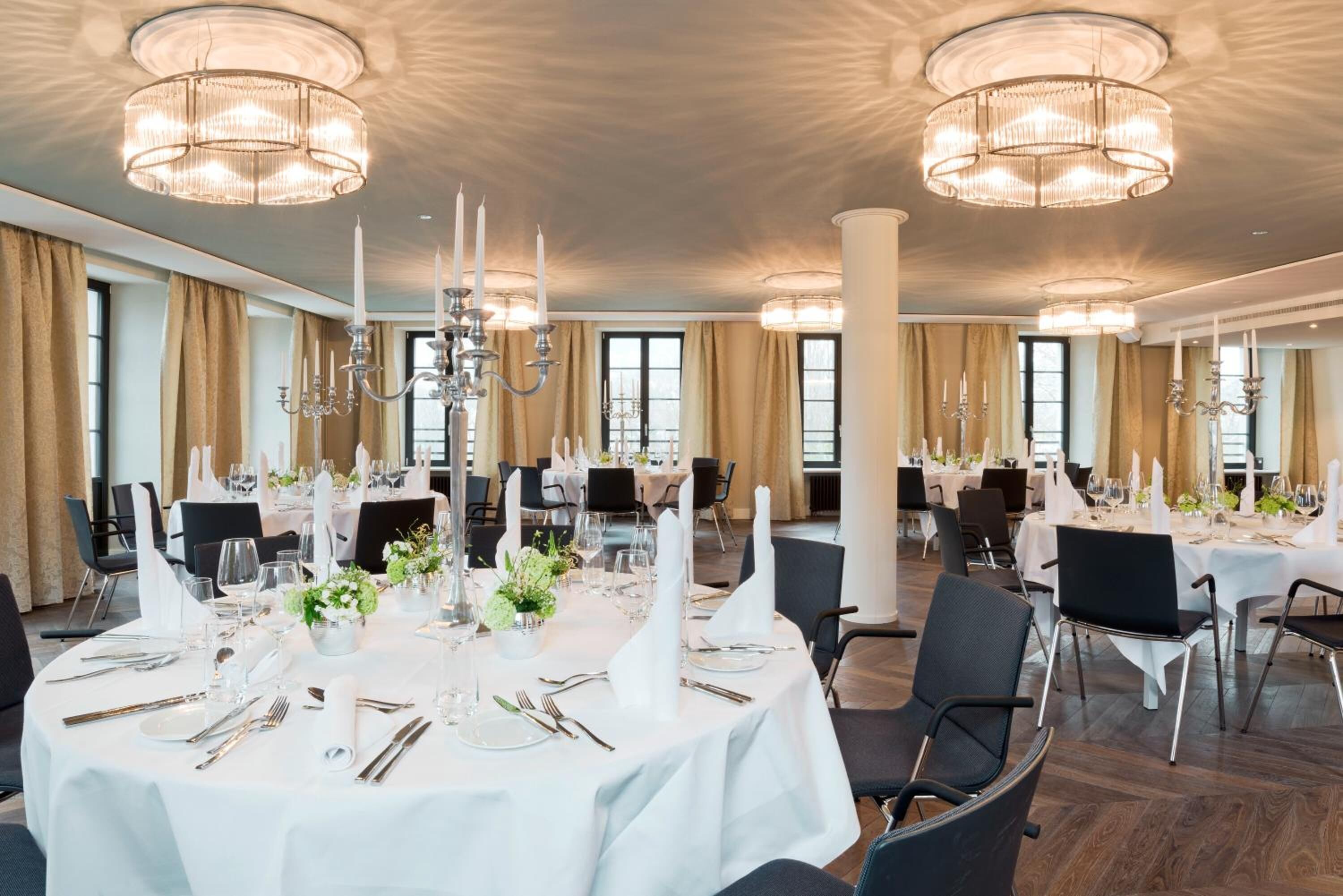 A banquet hall with round tables set for dining, large chandeliers, and tall columns.
