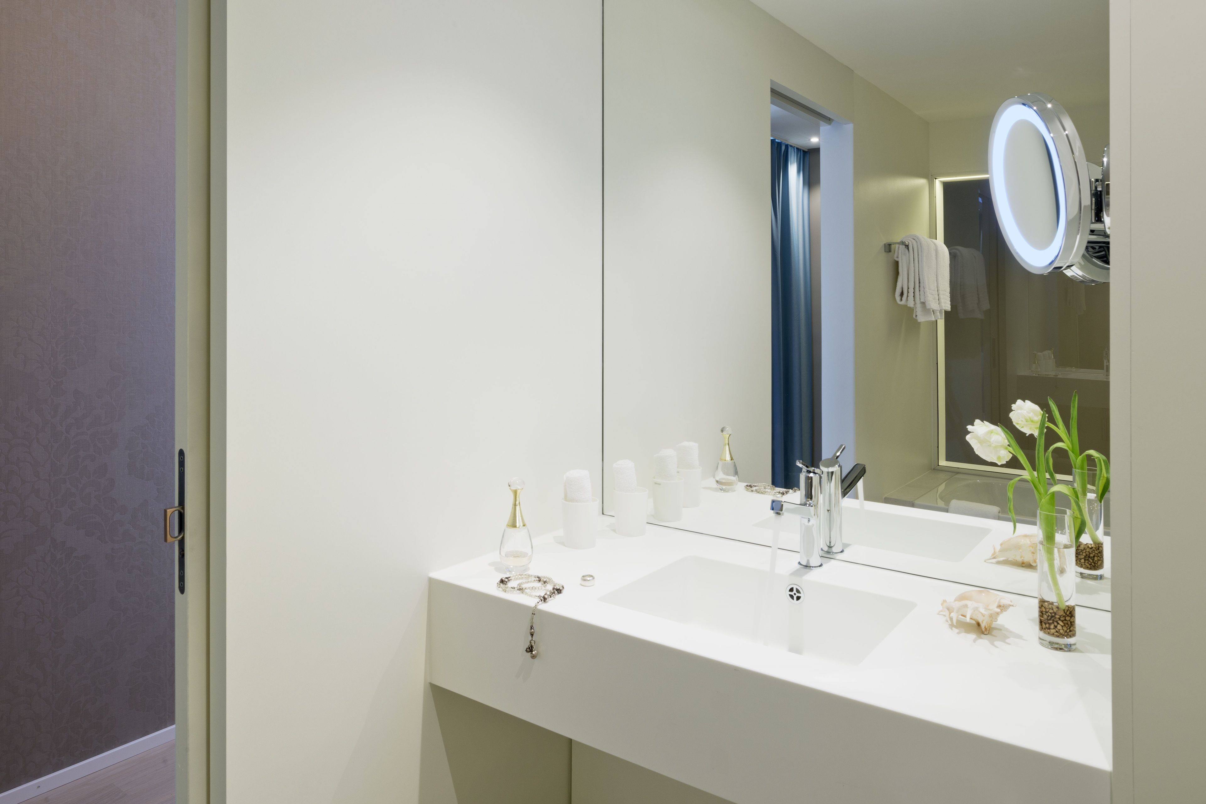 A modern bathroom with a white vanity, a large mirror, and a small vase with flowers.