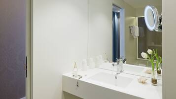 A modern bathroom with a white vanity, a large mirror, and a small vase with flowers.